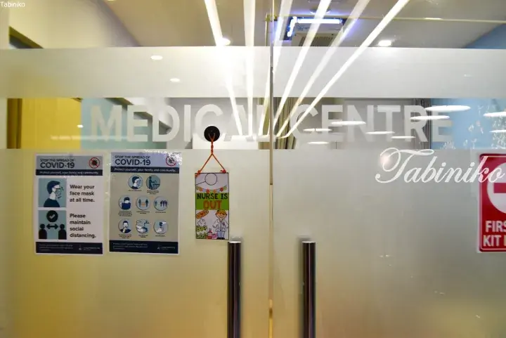 Glass door of a medical centre with COVID-19 safety posters and a &ldquo;Nurse is Out&rdquo; sign.