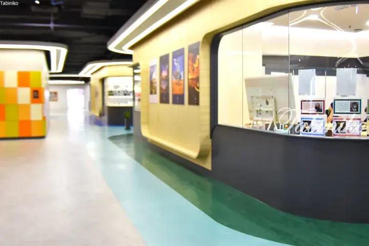 Modern interior hallway with curved wooden walls, colorful floor stripes, and glass-enclosed consultation booths.