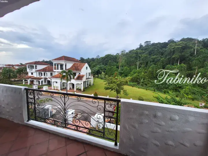 View from balcony overlooking white villas with terracotta roofs and lush green hillside in Malaysia