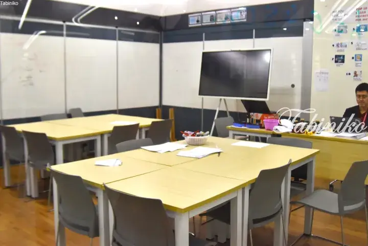Modern classroom with light wood tables, grey chairs, whiteboards, and a large screen in a Malaysia training center.
