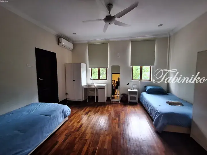 Bright bedroom with wooden floors, two single beds, desk, and wardrobe at Tabiniko hostel in Malaysia.