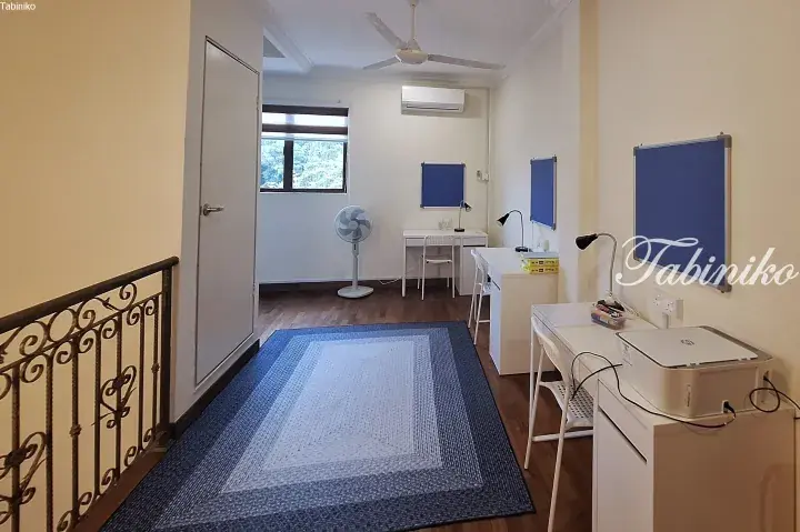 Bright shared study room with white desks, blue pinboards, ceiling fan, and hardwood floors.