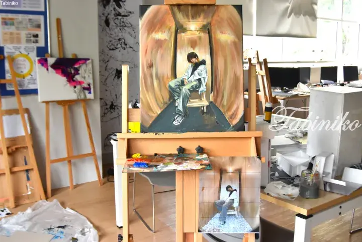 Oil painting of a person sitting in a hallway displayed on an easel in an art studio with other canvases and supplies.