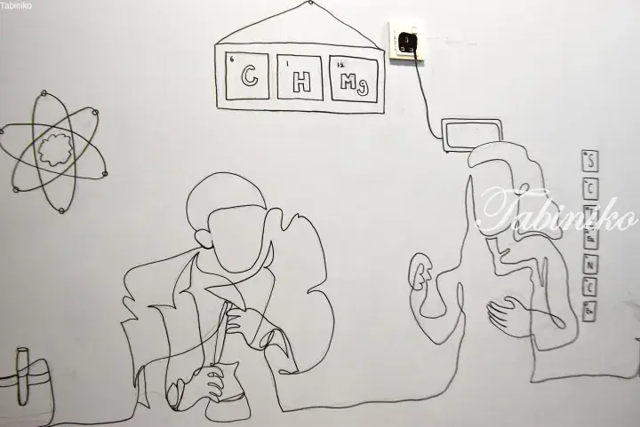 A line drawing showing two figures in a room with a periodic table sign reading &lsquo;CHMg&rsquo; and an atom symbol on the wall.