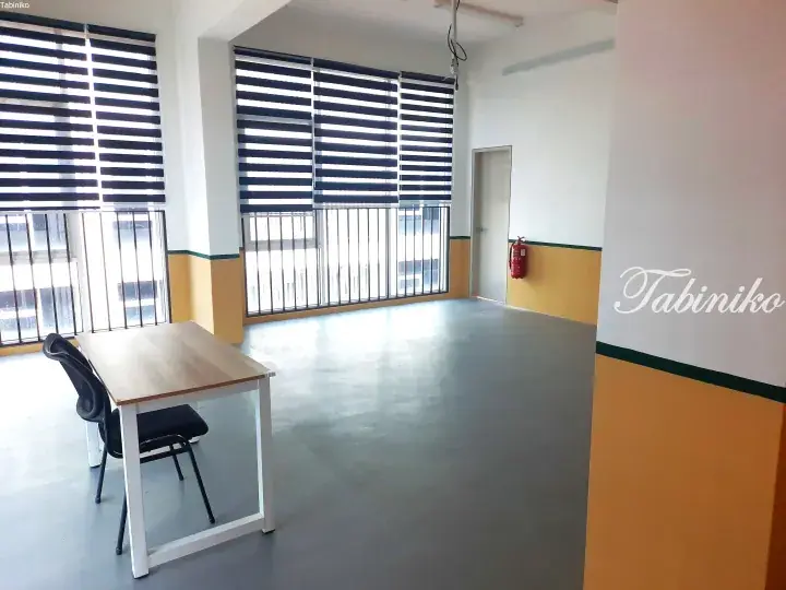 Bright empty office space with large windows, striped blinds, and a single desk and chair.