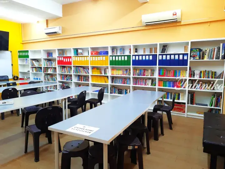Bright yellow-walled study room with white tables, black chairs, and organized bookshelves in a Malaysian educational facility.