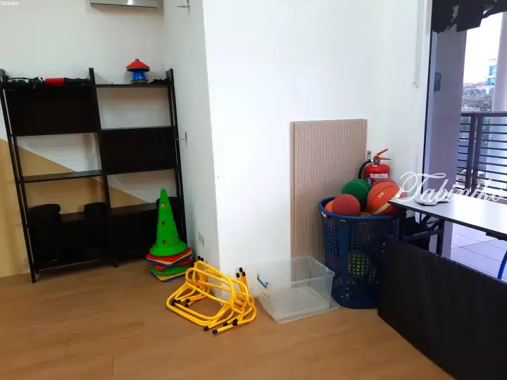 Colorful children&rsquo;s play equipment including cones, hurdles, and balls stored in a bright room with wooden flooring.