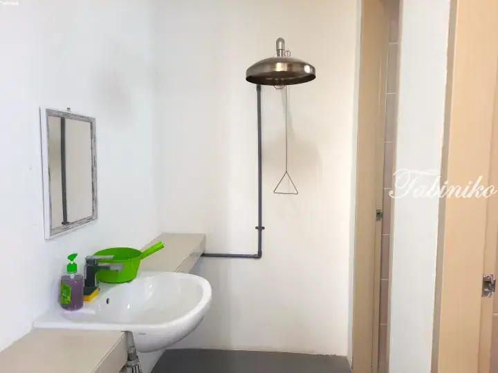 Modern bathroom with a white sink, mirror, and a distinctive overhead shower with a triangular pull chain.