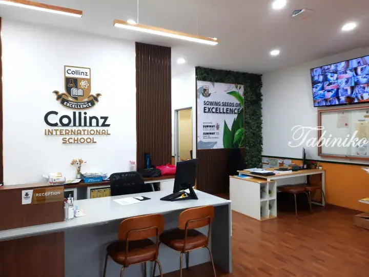 Reception area of Collinz International School featuring the school logo, a modern desk with chairs, and a security monitor display.