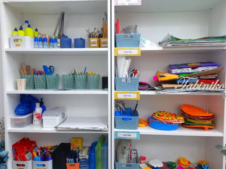 Organized classroom shelves displaying art supplies, labeled bins for Year Four and Five students, and colorful student artwork.