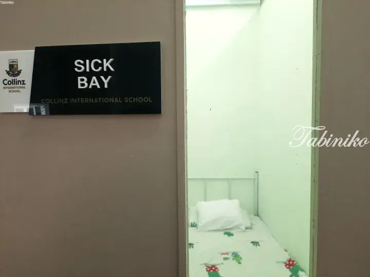 Sign for the Sick Bay at Collinz International School with a view of a bed inside.