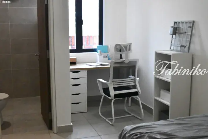 Bright bedroom with a white desk, ergonomic chair, and shelving unit near a window.