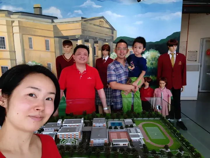 Family posing with a school campus model and mannequins wearing uniforms at a property exhibition.