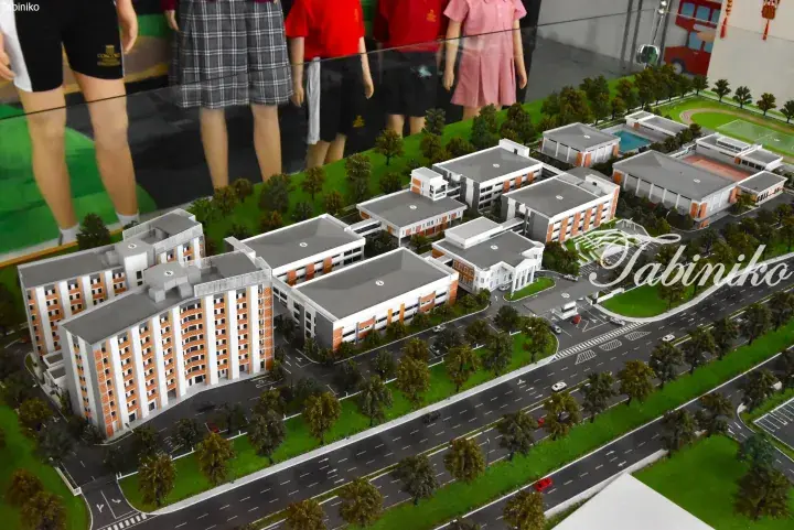 Architectural model of a modern school campus featuring orange and white buildings, sports fields, and student figures.