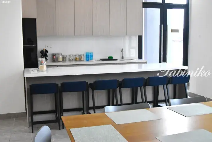 Modern kitchen with a white countertop, light wood cabinets, and blue bar stools in a Malaysian property.