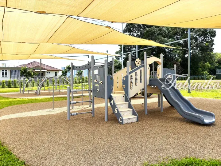 Modern playground with a slide and climbing frame under a yellow shade sail on a safety surface.