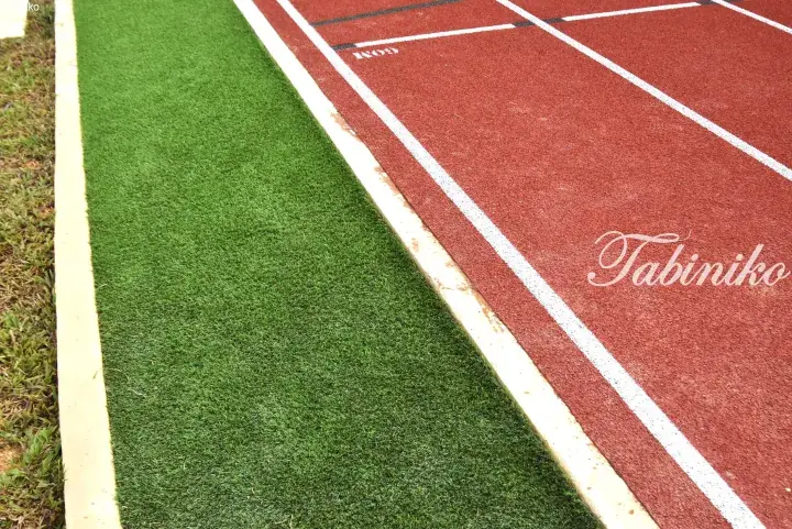 Close-up of a red running track with white lane lines next to green artificial turf at a sports facility.