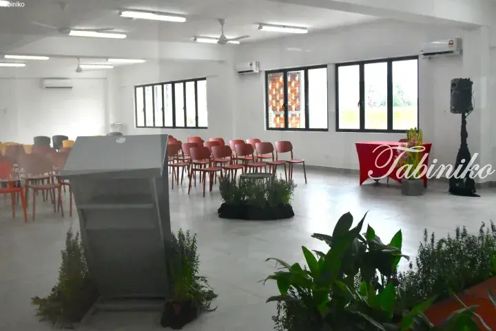Bright event hall with red chairs, podium, and plants, ready for a gathering.