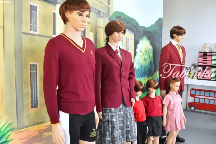 Mannequins display Concord College school uniforms in maroon and pink against a painted school building backdrop.