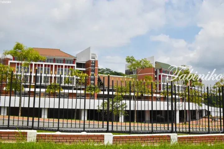 Modern red brick and white building with traditional tiled roofs behind a black metal fence with gold accents.