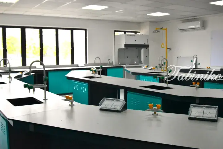 Modern laboratory with teal cabinets, white countertops, sinks, and a fume hood in a bright room.