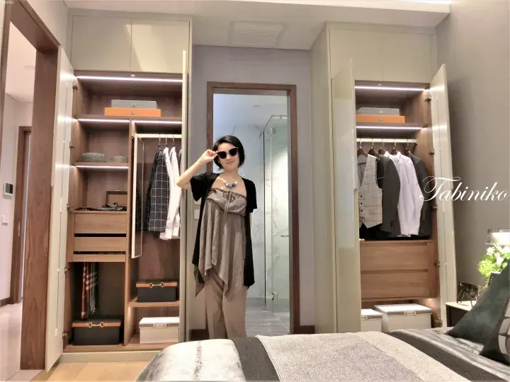Woman posing in a modern walk-in closet with open wardrobes and organized clothing in a luxury Malaysian home.