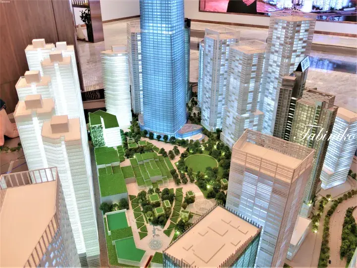 Architectural model of a modern high-rise development with a central green park and surrounding skyscrapers.