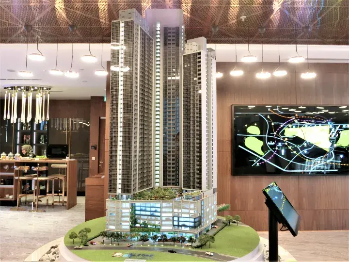 Architectural model of a modern high-rise residential development with a digital location map display in the background.