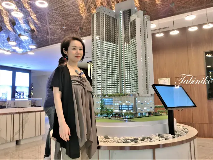 Woman standing beside a detailed architectural model of high-rise condominiums at a property showroom.