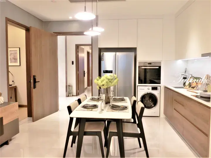 Modern dining area with white table, black chairs, and kitchen featuring stainless steel fridge and built-in oven.