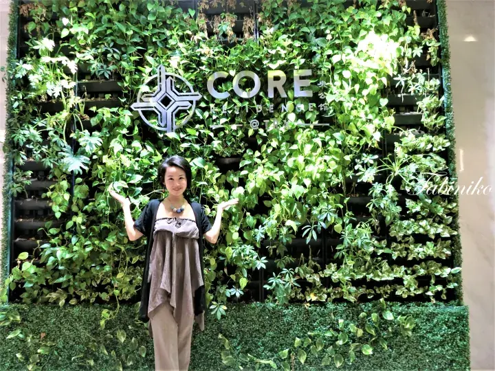 Woman posing in front of a lush green vertical garden wall featuring the CORE Residence @ TRX logo.