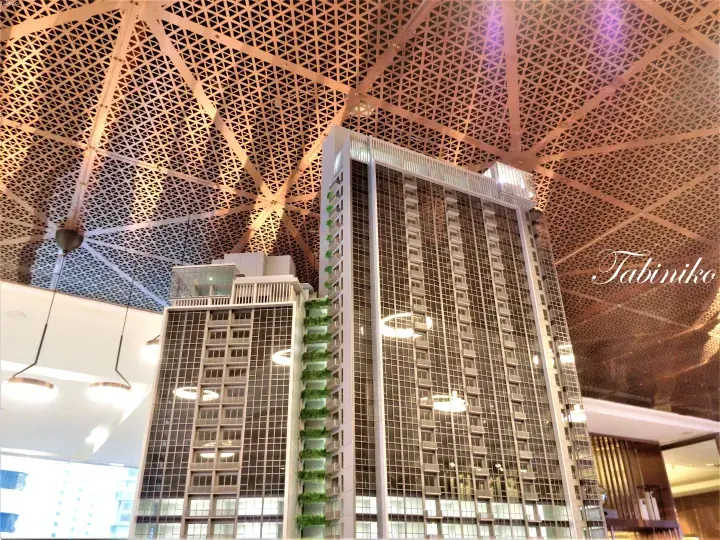 Architectural model of a modern high-rise building with a geometric lattice ceiling backdrop.