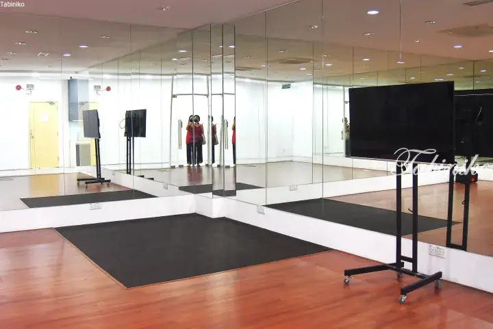 Spacious dance studio with floor-to-ceiling mirrors, wooden flooring, and a large TV on a mobile stand.