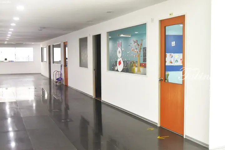 Bright hallway in a Malaysian childcare center with glossy floors, orange doors, and a classroom window featuring a rabbit decoration.