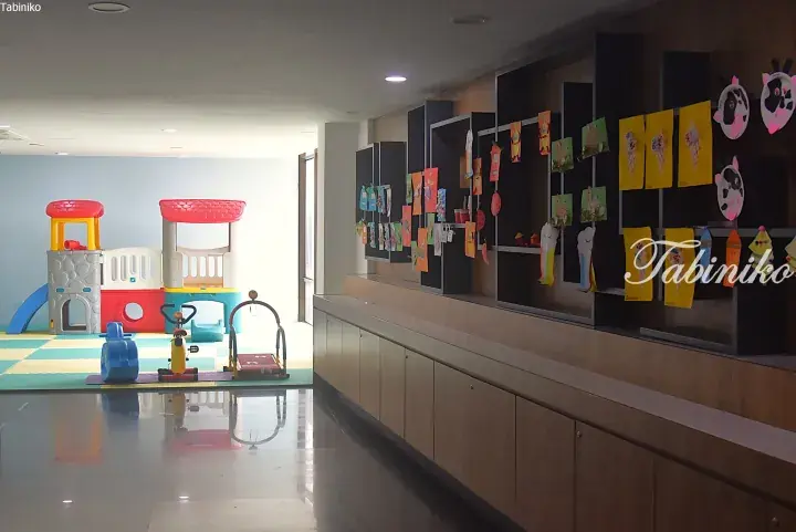 Indoor children’s play area with colorful plastic castle and ride-on toys, next to a wall displaying kids’ artwork.