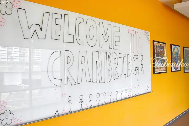 Whiteboard sign welcoming visitors to Cranbridge, a property in Malaysia, decorated with simple stick figures and flowers.