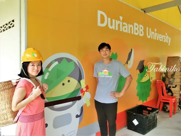 Couple posing at DurianBB University with a durian mascot and yellow helmet.