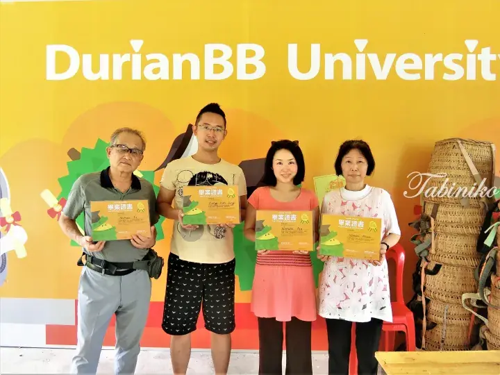 Four people holding graduation certificates in front of a DurianBB University sign.