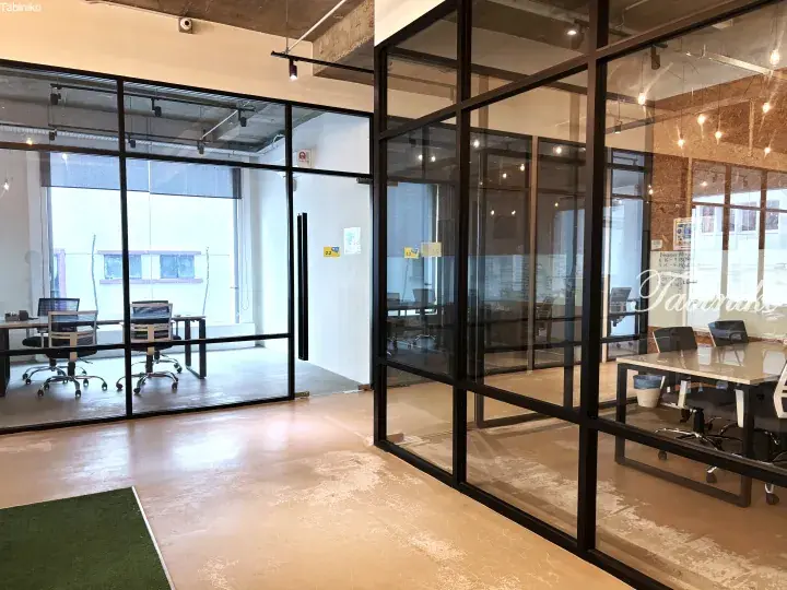 Modern office space with glass partitions, concrete floors, and natural light in a Malaysian co-working environment.