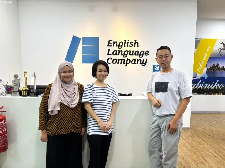 Three people standing in front of the English Language Company reception desk with awards displayed on the counter.
