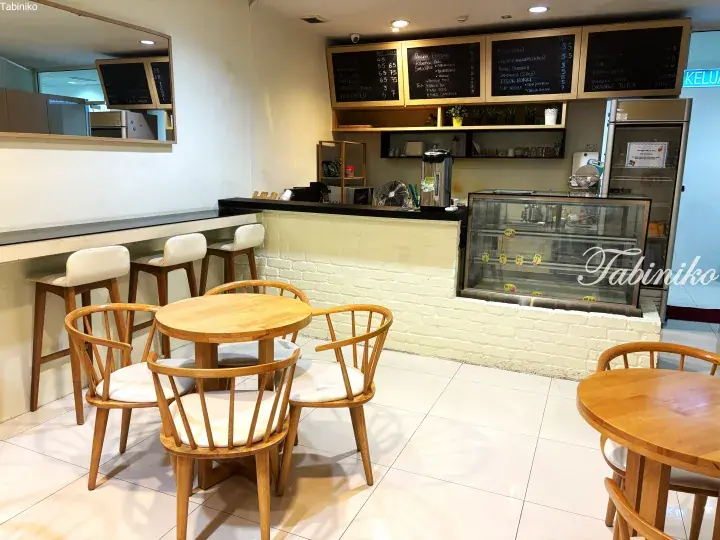 Cozy cafe interior with wooden tables, white chairs, and chalkboard menu displaying coffee and snacks.