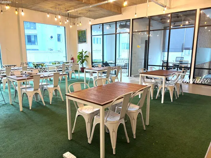 Bright coworking space with wooden tables, white chairs, and green carpet in a modern office setting.