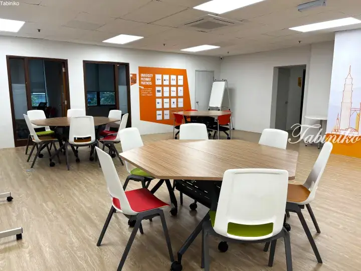 Modern study room with wooden tables and colorful chairs, featuring a University Pathway Partners display board.