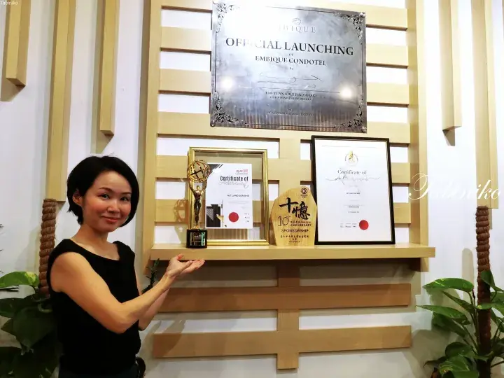 Woman proudly displaying awards and the official launch plaque for Embique Condotel in Melaka.