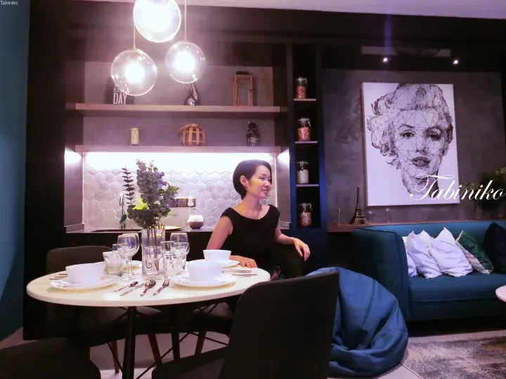 Woman seated at a modern dining table in a stylish apartment with hexagonal tiles and geometric wall art.