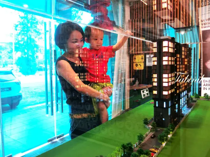 Woman holding a child looking at a detailed architectural model of a modern residential building in a sales gallery.