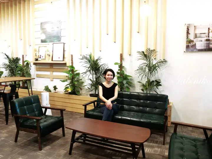 Woman sitting on green leather sofa in modern office lounge with plants and wooden accents