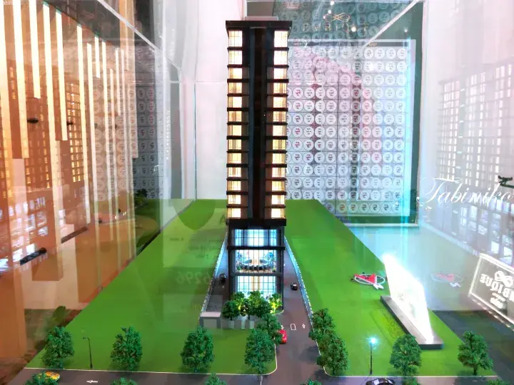 Architectural model of Embique condominium tower with illuminated windows and landscaped green surroundings.