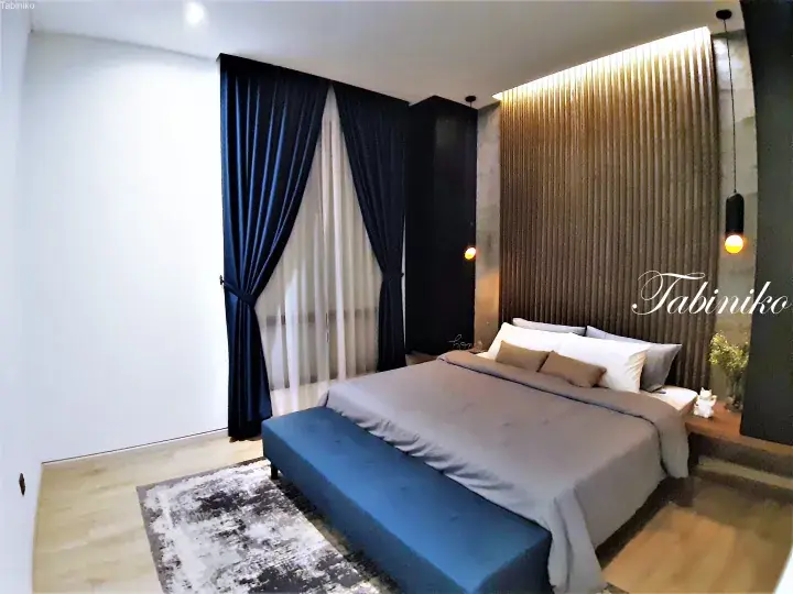 Modern bedroom with a wooden slat headboard wall, blue velvet bench, and navy curtains.