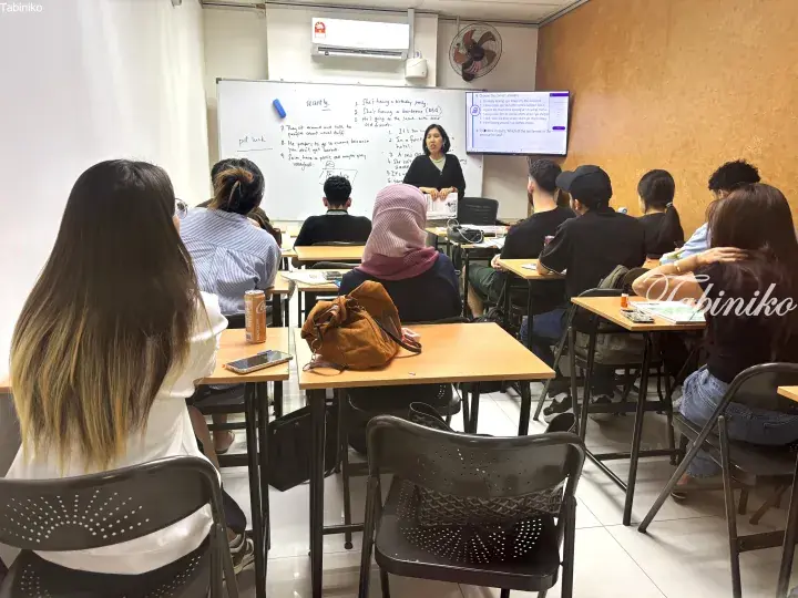 English language class in a Malaysia classroom with students listening to a teacher at the whiteboard.